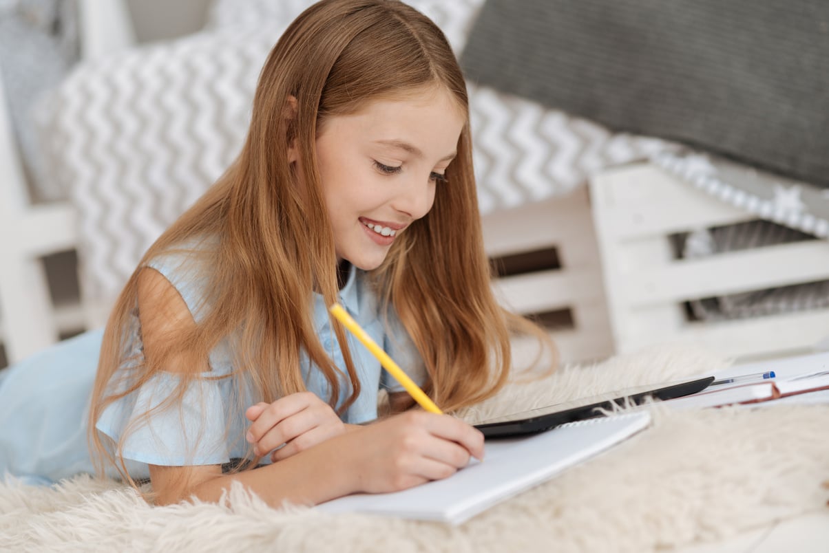 Adorable kid writing in notebook while studying at home